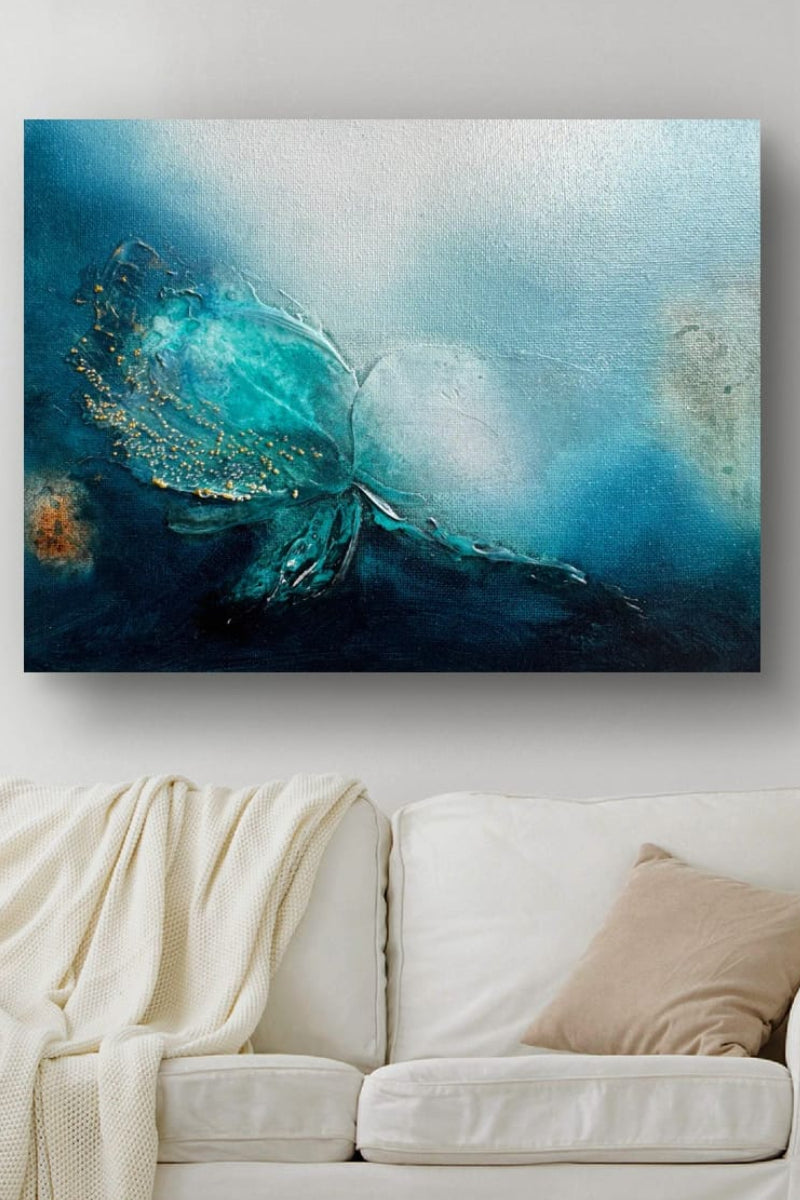 Abstract canvas wall art featuring a butterfly in shades of teal, blue, and black, displayed on a light gray wall above a white sofa with a cream throw blanket.
